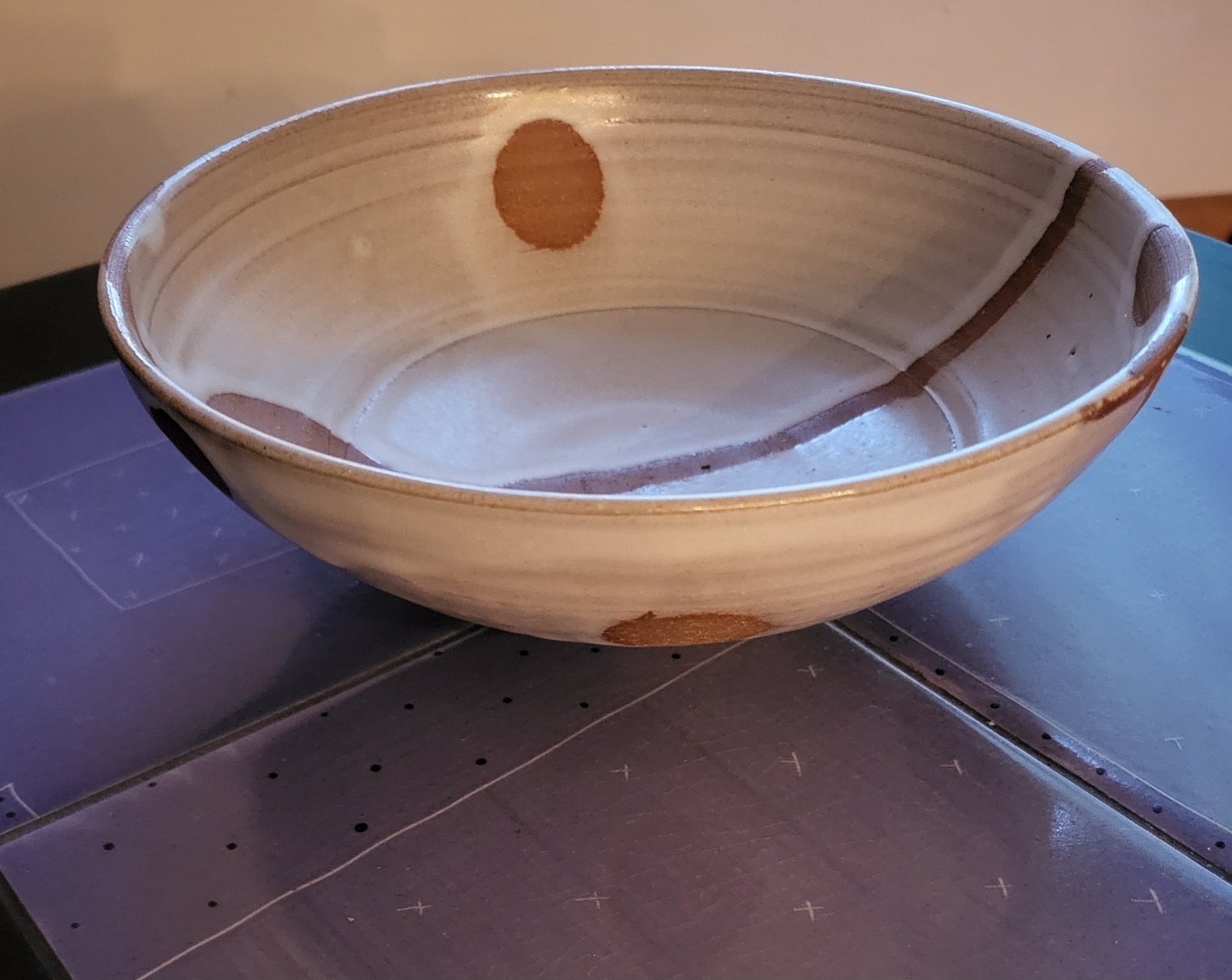 A wide shallow stoneware bowl with an ivory glaze and warm rust-colored ovoid spots and a vertical trail.
