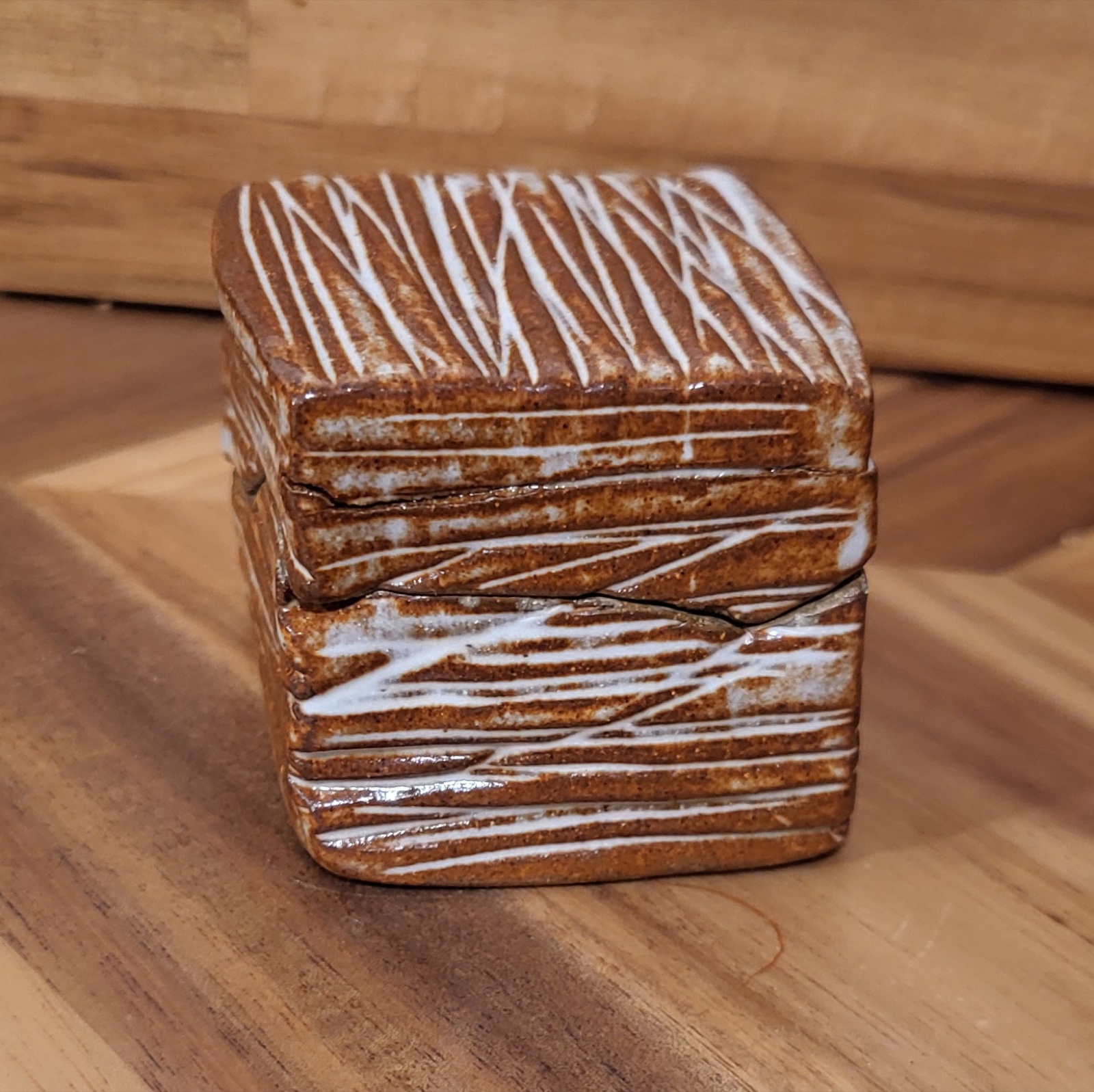 A small lidded stoneware box with white combed slip lines over a warm earth-tone clay body.